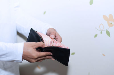 Midsection of man hands holding wallet against wall