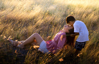 Side view of two son kissing mother sitting on land