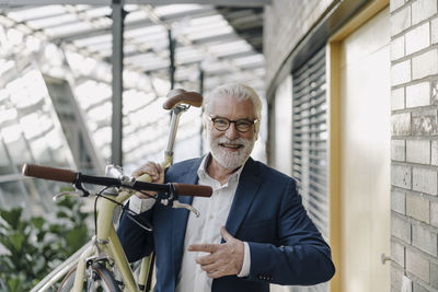 Portrait of a happy senior businessman with a bike in a modern office building