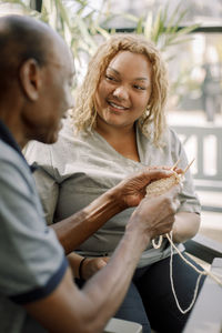 Smiling female nurse assisting senior man in crocheting at retirement home