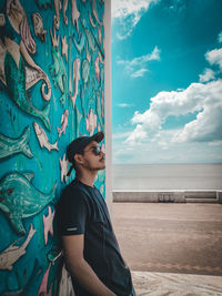 Side view of young man looking at sea against sky