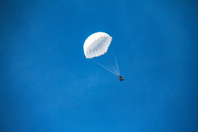 Low angle view of people parasailing in blue sky