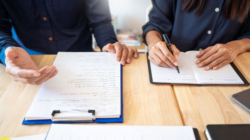 Midsection of businesswoman and colleague working on table