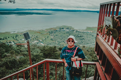 Portrait of smiling woman standing on railing against sea