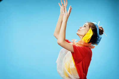 Side view of woman looking up while standing against blue background