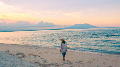 Young woman looking away while standing at beach during sunset