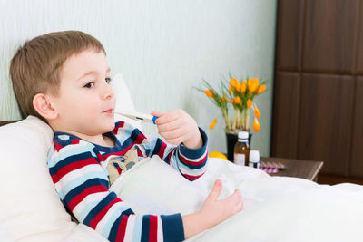 Cute boy holding thermometer in mouth at home