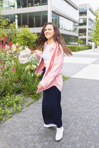 Happy young woman in pink shirt turning around with backpack on street