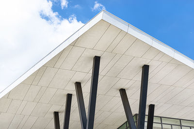 A modern concrete roof supported by steel pillars against a blue sky with clouds.