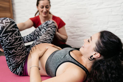 Fitness instructor assisting pregnant woman while exercising at home