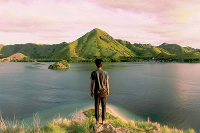 Rear view of man looking at lake during sunset