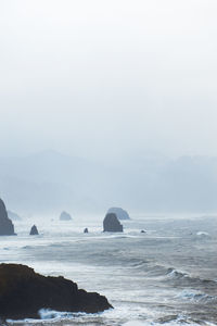 Rock formation in sea against sky during foggy weather