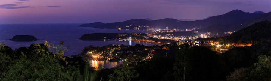 High angle view of illuminated city by sea against sky at night