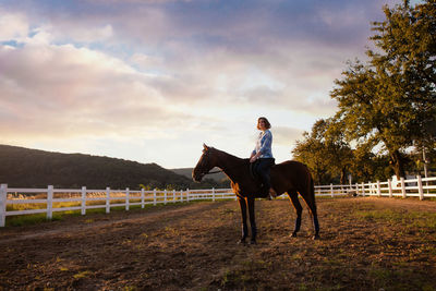 Man riding horse in ranch against sky