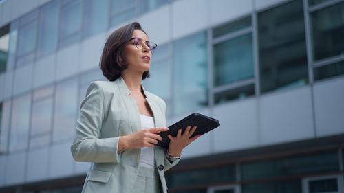 Pretty caucasian woman in glasses having video chat on tablet device outdoor at business building