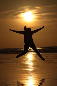 Silhouette woman jumping on beach against sky during sunset