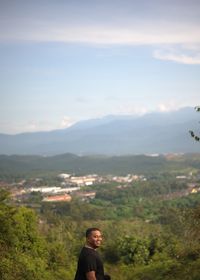 Portrait of young man standing on mountain against sky