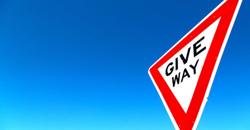 Close-up of road sign against clear blue sky