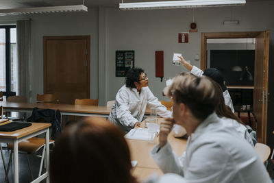 Teacher examining chemical in beaker with students at laboratory