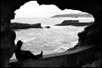 Man sitting on retaining wall against sea