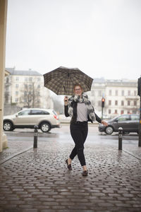 Portrait of young woman carrying umbrella on footpath