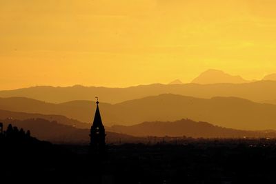 Silhouette building and mountains against orange sky