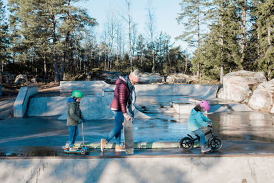 Mom and her kids walking across a skatepark with bikes and scooters