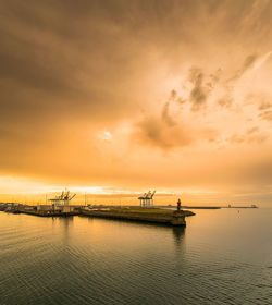 Drilling rig against cloudy sky during sunset