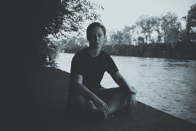 Full length portrait of young man sitting on retaining wall by river