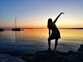 Silhouette woman standing on rock at beach against sky