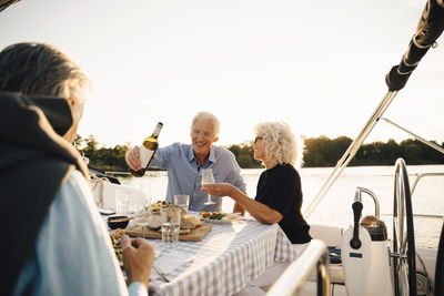 Cheerful senior friends having wine while spending leisure time in sailboat