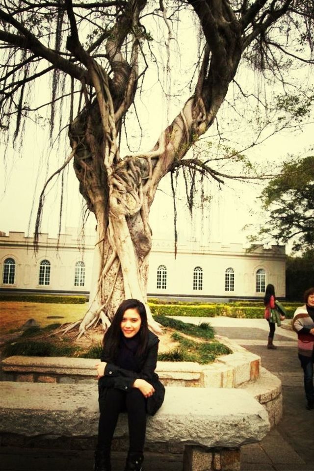 lifestyles, leisure activity, young adult, tree, casual clothing, architecture, building exterior, bare tree, built structure, person, young women, standing, full length, looking at camera, smiling, front view, sky, portrait