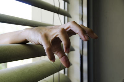 Cropped hand of woman amidst window blinds