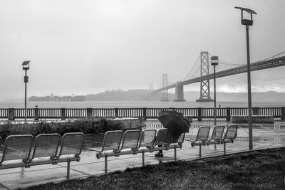 Person with umbrella by bay bridge against sky during rainy season