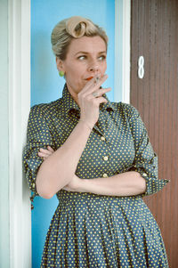 Mature woman smoking cigarette while standing against door