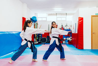 Full length of young woman with instructor practicing martial arts