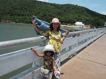Portrait of mother and daughter standing by railing over river