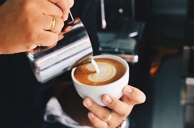Close-up of hands pouring milk in coffee