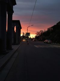 Empty road by buildings against sky during sunset