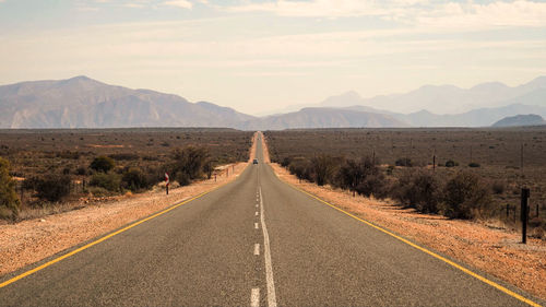 Empty road along landscape and mountains against sky