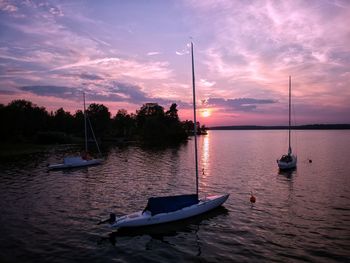 Sailboats moored in lake against sky during sunset