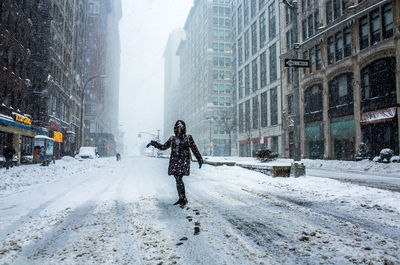 Full length of woman standing on street amidst buildings during snowfall