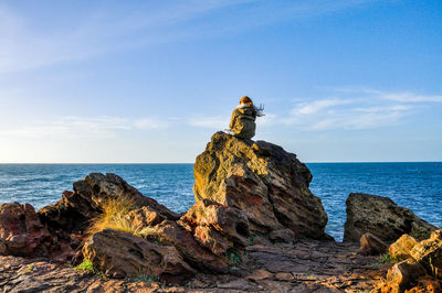 Girl sitting on rock formation on beach against sky