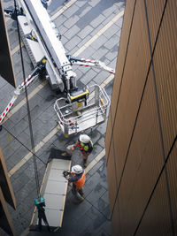 Two workmen prepare hoisting operation of a building panel using a mechanical crane. 