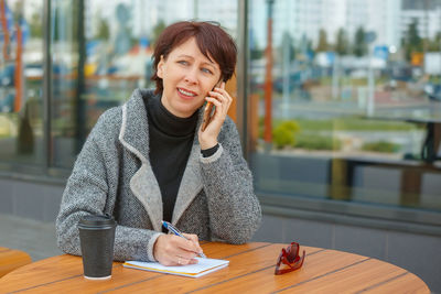 Young woman using phone while sitting on table