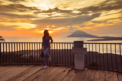 Full length of woman leaning on railing at observation point during sunset