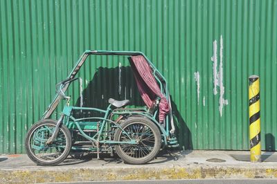 Tricycle parked by corrugated iron