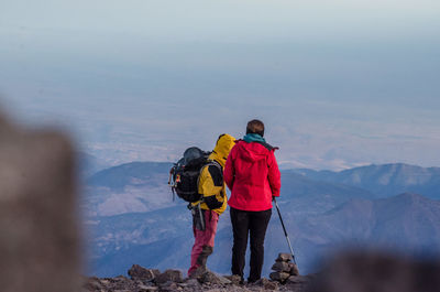 Rear view of men on mountain against sky during winter