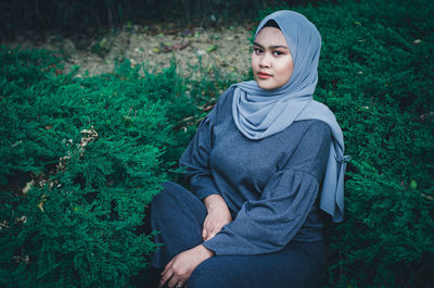 Portrait of young woman in hijab sitting amidst plants on field
