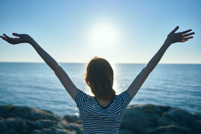 Rear view of woman with arms raised against sea